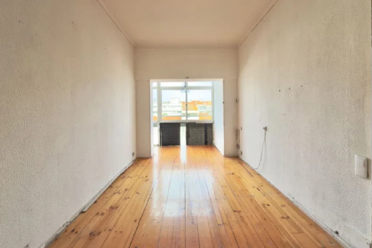 An empty apartment living room with bare walls, a wooden floor and a loose cable on the right wall